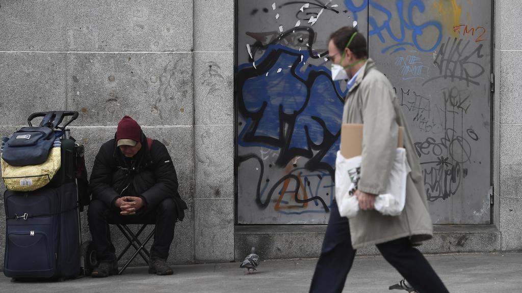 homme masqué marchant dans la rue masqué à côté d'une personne sans abris