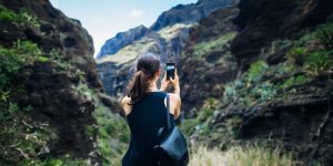 Young woman taking photo of mountains landscape using phone, Canary islands Spain. Travel concept